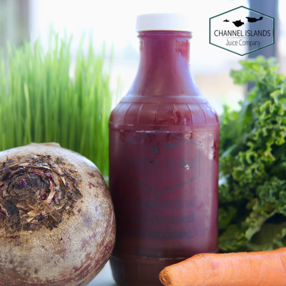 A bottle of cold-pressed juice beside fresh beets, carrots, kale and wheatgrass