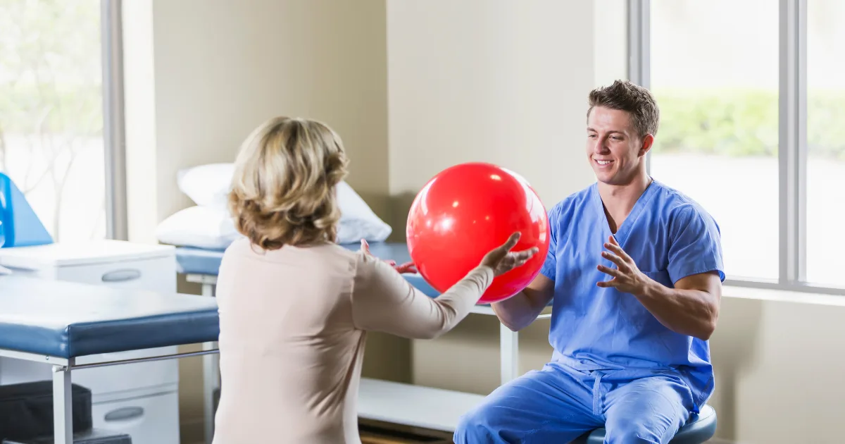 Physical therapist working with a patient on a ball exercise in a bright clinic